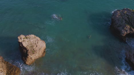 Tilt-up-aerial-drone-clip-moving-over-a-sandy-beach-and-a-rock-formation-in-Kavala,-Macedonia,-Greece