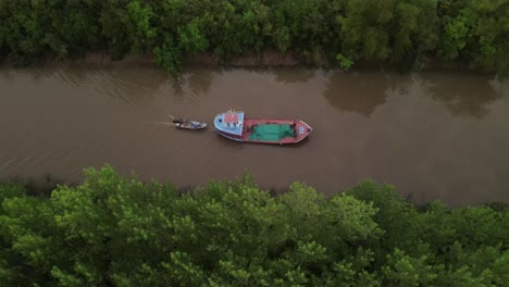 Cinematic-drone-side-shot-of-ship-carrying-small-boat-on-amazon-river-surrounded-by-green-rainforest-trees-during-sunrise
