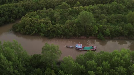 Cinematic-drone-side-shot-of-ship-carrying-small-boat-on-amazon-river-surrounded-by-green-rainforest-trees-during-sunset