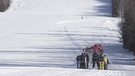 Rotes-Pistenfahrzeug,-Das-Eine-Gruppe-Von-Skifahrern-Bergauf-Eine-Skipiste-Schleppt,-Tschechien