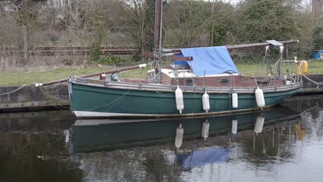 Old-wooden-sailboat-moored-on-narrow-rural-countryside-canal-marina