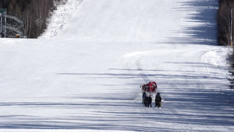 Rotes-Pistenfahrzeug,-Das-Eine-Gruppe-Von-Skifahrern-Auf-Eine-Verschneite-Skipiste-Schleppt,-Tschechien