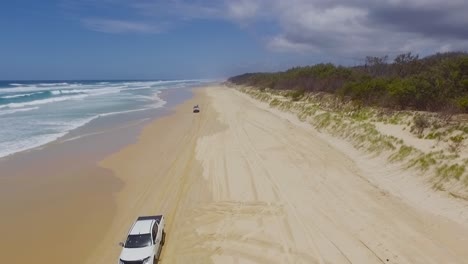 Low-aerial-drone-shot-looking-south-down-North-Stradbroke-Island's-Main-Beach-as-4x4-four-wheel-drive-trucks-and-cars-drive-beneath-our-vantage-point
