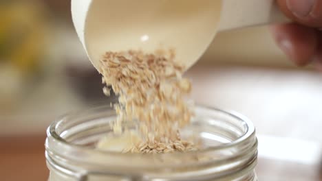Hand-Pouring-Oat-Flakes-in-Glass-Jar,-Slow-Motion,-Extreme-Close-Up-View