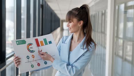 Pretty-woman-in-business-suit-shows-on-slide-with-infographics-looking-at-camera