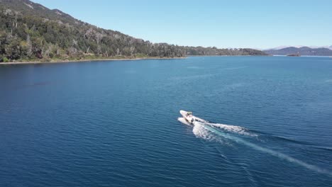 Tracking-aerial-follows-bright-white-motorboat-speeding-on-blue-lake