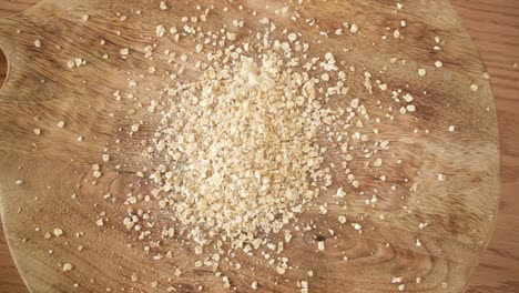 Dropping-Oat-Flakes-into-Heap-on-Wooden-Background,-Top-Down-View,-Slow-Motion
