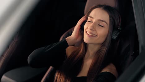 Portrait-of-a-young-beautiful-girl-sitting-in-the-car-listening-to-music-on-headphones