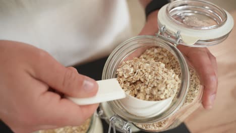 Person-Scoops-Spoonful-of-Oat-Flakes-From-Jar,-Slow-Motion-Close-up