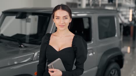 Beautiful-young-woman-in-a-business-suit-looks-at-the-camera-and-smiles-on-the-background-of-the-car