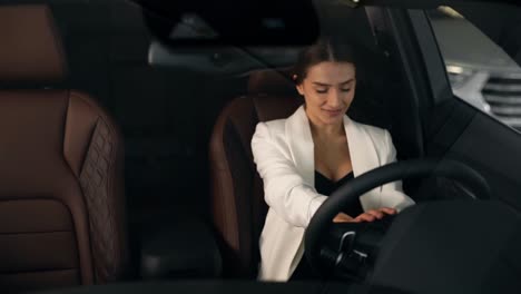 Beautiful-smiling-girl-sitting-behind-the-wheel-of-an-elegant-car-evaluates-the-steering-wheel