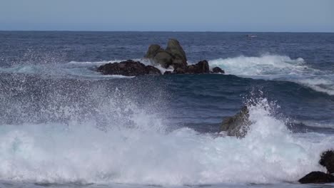 Incoming-waves-break-violently-on-shore-rocks,-splashing-up-sea-foam