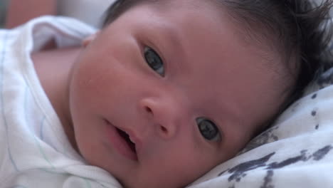 Close-Up-Of-Cute-Newborn-Baby's-Face-Lying-Awake-In-Bedroom