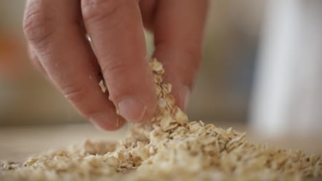 Hand-Grabs-Oat-Flakes-and-Drops-in-Pile,-Slow-Motion-Close-Up-with-Copy-Space