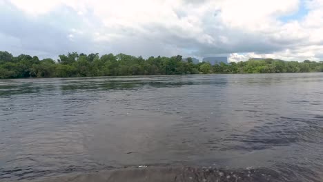 Slow-motion-shot-of-the-wake-of-a-canoe-with-the-jungle-and-amazing-tepuy-mountains-at-the-back,-in-the-Carrao-River,-in-Canaima,-Venezuela