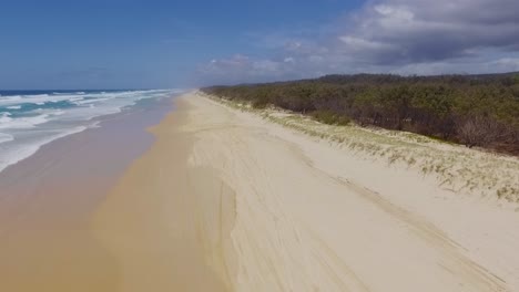 Smooth-and-slow-rising-aerial-drone-shot-looking-South-over-the-dunes-and-bushland,-down-a-deserted-Main-Beach,-on-North-Stradbroke-Island-in-Sunny-Queensland,-Australia