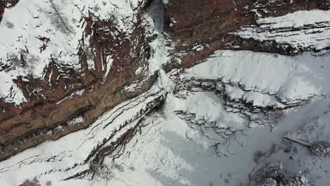 Drone-aerial-view-of-frozen-waterfall-on-rocky-cliff-in-snowy-winter-landscape