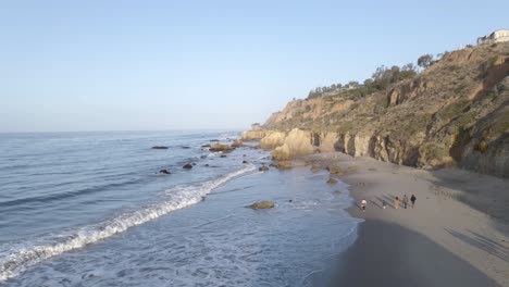 People-walking-on-El-Matador-beach-at-sunrise,-Malibu-in-California