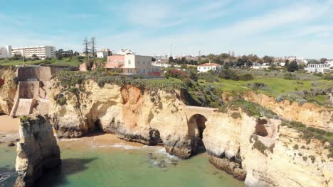 Idyllic-Estudante-Beach-ocean-front-with-Roman-bridge-near-coastline,-Algarve,-Portugal---Aerial-Fly-over-push-in-shot