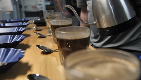 Hot-steamy-water-is-poured-for-coffee-cupping-taste-test,-slow-motion-close-up