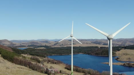 Drone-aerial-view-of-wind-turbines-by-norwegian-fjord-on-sunny-day,-alternative-renewable-power-energy-concept