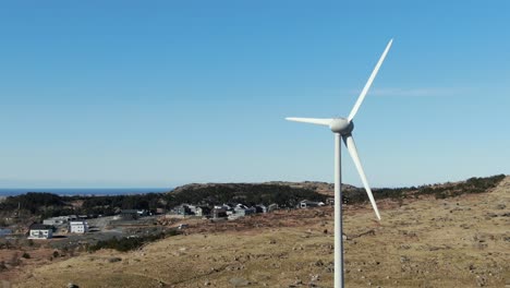 Drone-aerial-view-of-windturbine-on-sunny-day-in-landscape-of-coastal-village-of-Norway,-alternative-sustainable-power-energy-concept