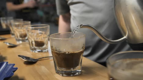 Pouring-hot-steamy-water-for-coffee-cupping-taste-test,-slow-motion-close-up