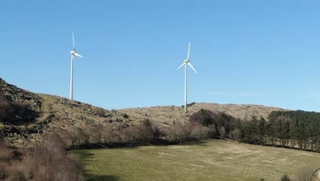 Drone-Aerial-View-of-Two-Wind-Turbines-in-Green-Landscape-on-Sunny-Day-Renewable-Alternative-Sustainable-Power-Energy-Concept