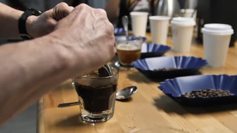 Scraping-top-layer-during-coffee-cupping-using-two-spoons,-slow-motion-close-up