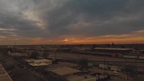 Filmische-Top-City-Luftaufnahme-Der-Innenstadt-Von-Roseville,-Kalifornien,-Mit-Industriegebäuden,-Geschäften-Und-Einem-Güterzug,-Der-Die-Eisenbahn-Hinunterfährt,-Mit-Einem-Leuchtend-Orangefarbenen-Sonnenuntergang-Im-Hintergrund