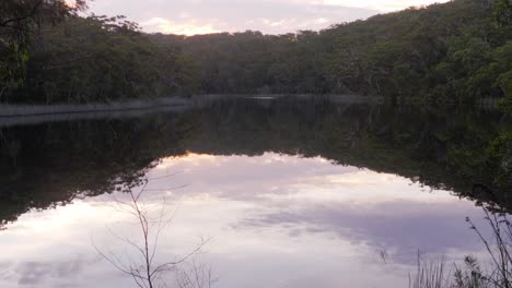 Calm-Lake-With-Cloudy-Sky-And-Lush-Foliage-Reflecting-On-Water-In-Blue-Lake-National-Park,-North-Stradbroke-Island,-Queensland,-Australia---tilt-up-shot