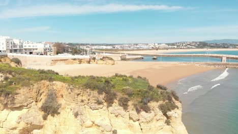 Playa-De-Batata-Bloqueada-Por-Acantilados-Erosionados-Y-Muelle-De-Solaria-En-Lagos,-Algarve,-Portugal---Toma-De-Seguimiento-De-Diapositivas-Aéreas