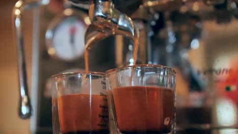 Espresso-machine-pouring-coffee-into-two-measuring-cups,-slow-motion-close-up
