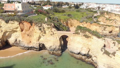 Roman-style-bridge-connecting-rock-outcrops-of-Lagos-Shoreline,-Algarve,-Portugal---Aerial-Point-of-interest-panoramic-shot
