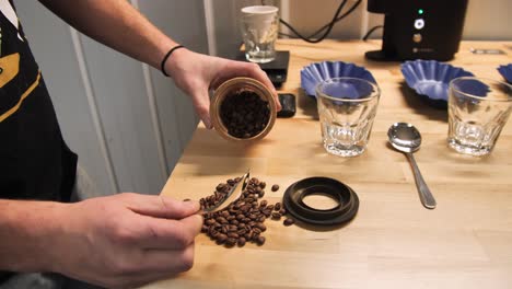 Man-pouring-out-coffee-beans-onto-a-table-top,-slow-motion-medium-shot