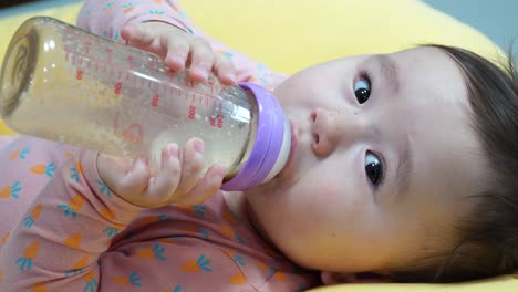 Cute-Baby-Girl-Lying-Down-And-Drinking-A-Bottle-Of-Milk---close-up