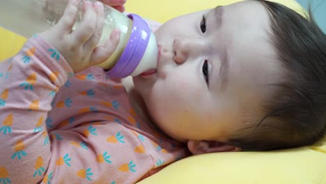 Hungry-Baby-drinking-formula-milk---holding-bottle-in-both-hands-and-looking-into-the-camera