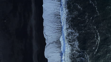 White-surf-waves-rolling-on-black-sand--top-view