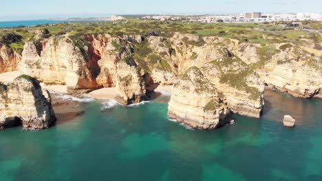 Intimate-sandy-coves-surrounded-by-towering-eroded-cliffs-in-Lagos,-Algarve,-Portugal---Aerial-wide-fly-back-shot