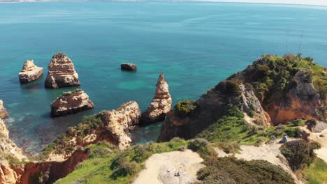 Sandstone-cliffs-shrouded-in-lush-green-grass-encircled-by-Algarve-Idyllic-sea---Aerial-slow-orbit-fly-over-shot