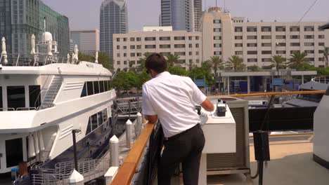 Ship-captain-master-in-uniform-docking-the-vessel-into-its-dock-in-the-city-of-San-Diego,-California-on-a-sunny-day