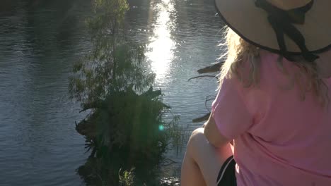 Outdoor-nature-blonde-woman-sitting-in-river-edge-wearing-pink-top-camping