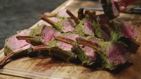 Chef-lays-out-venison-meat-ribs-slices,-with-green-spice-on-top,-on-wooden-cut-board