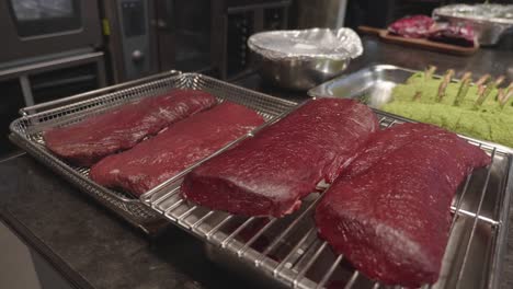 Big-Venison-meat-slices-on-a-metal-tray-on-kitchen-table,-before-baking-in-oven