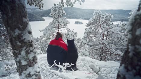 Rückansicht-Eines-Mannes-Mit-Seinem-Alaskan-Malamute-Hund,-Der-In-Einem-Schneebedeckten-Berg-In-Norwegen-Sitzt---Weitschuss