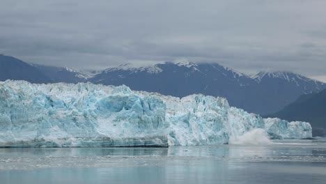 Aufnahmen-Zur-Erwärmung-Des-Globalen-Klimawandels:-Gletscherbrocken-Schmelzen,-Kalben-Und-Fallen-In-Alaska-An-Einem-Dunklen,-Düsteren,-Bewölkten-Tag-Mit-Schneebedeckten-Bergen-Im-Hintergrund