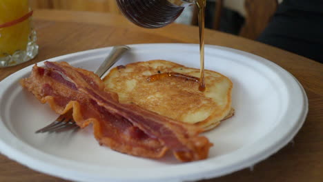 Maple-syrup-being-poured-on-a-freshly-fried-pancake-with-two-slices-of-bacon---slow-motion