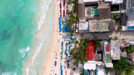 Cinematic-downward-drone-shot-lowering-towards-the-people-on-the-beach-in-Playa-Del-Carmen-Mexico,-clear-blue-ocean-water