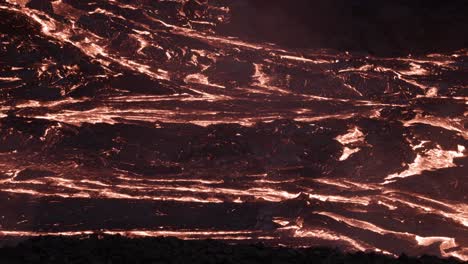 Dark-wrinkle-surface-on-slow-flowing-lava-river-at-night,-active-volcanic-field