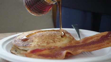 Pouring-warm-maple-syrup-on-a-short-stack-of-pancakes-for-a-traditional-American-breakfast---slow-motion